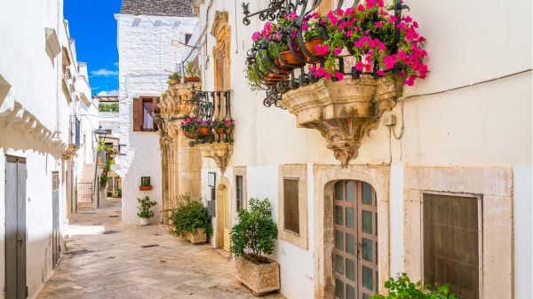 Wąska uliczka w Apulii z kwiatami na balkonach i białą zabudową